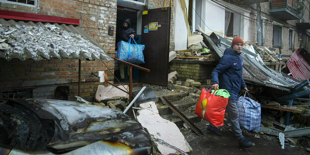 Zwei Männer gehen mit Tüten beladen aus einem schwer beschädigten Haus