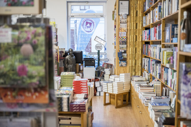 Blick in die Buchhandlung, mit Regalen, Postkartenständer, und Bücherstapeln