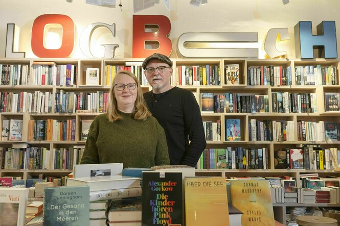 Die beiden InhaberInnen Sabine und Axel Stiehler stehen in ihrer Buchhandliung hinter einem Bücherregal und vor einem Büchertisch