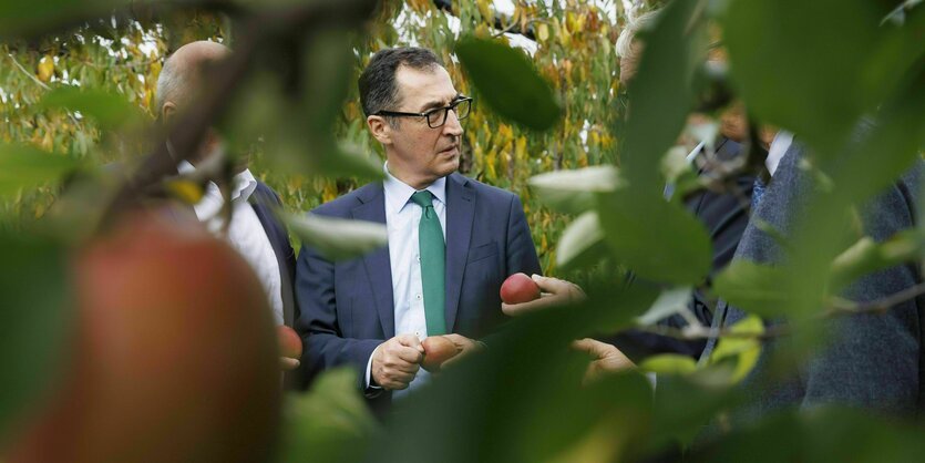 Cem Özdemir steht zwischen Bäumen mit einem Apfel in der Hand