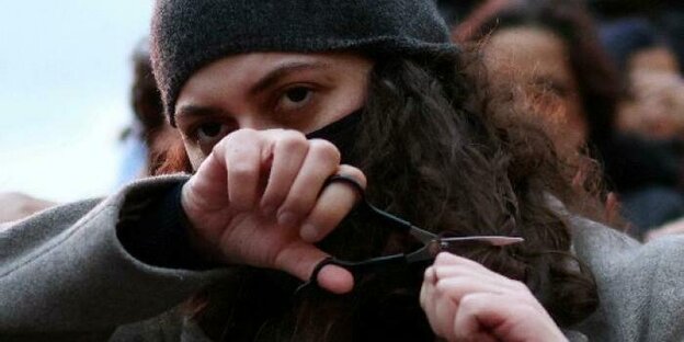 Eine Demonstrantin mit schwarzem Kopftuch schneidet sich eine Stähne ihres Haares ab, das unter dem Tuch hervorguckt