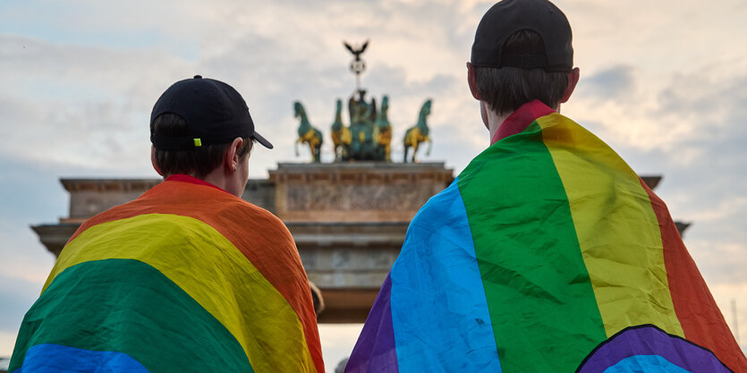 Zwei Personen mit Regenbogenfahnen vor dem Berliner Brandeburger Tor