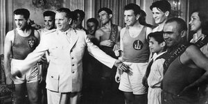 Eine Gruppe von Personen in Sportbekleidung steht um einen Mann in weißer Uniform herum