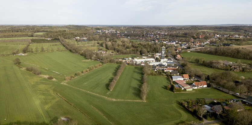 Ein Luftbild zeigt Wiesen, ein Dorf mit Kirchturm im Hintergrund und Wälder