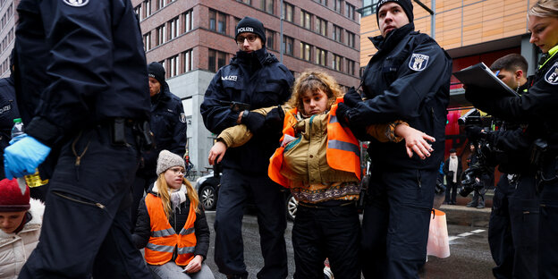 Polizist*innen tragen eine Aktivistin der Letzten Generation weg