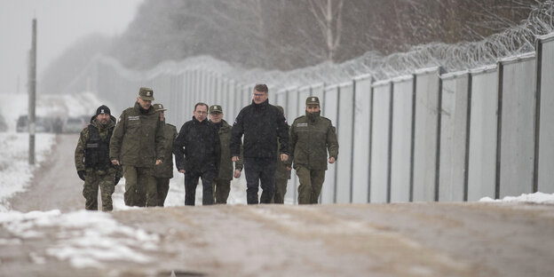 mehre Soldaten gehen im Winter an einem Grenzzaun entlang