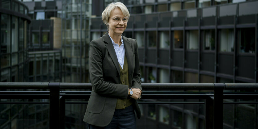 Dorothee Feller steht in dunklem Jacket vor einem dunklen Gebäude und lehnt sich mit dem Arm an ein Gelände