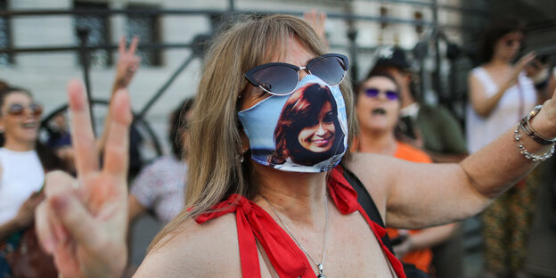 A woman wearing a mask with a portrait of Kirchner printed on it makes the victory sign