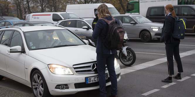 Zwei Aktivist*innen stehen vor einer Reihe stehender Autos und halten den Verkehr auf