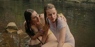 Grace (Maiah Stewardson) und Claudia (Markella Kavenagh) kauern beim Baden am Ufer.