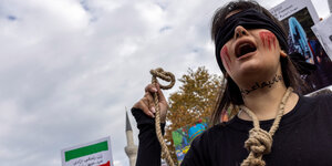 Eine Frau auf einer Demonstration, sie trägt eine Augenbinde und einen Strick um den Hals