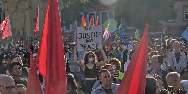 Menschen mit Fahnen und Schildern bei einer Demonstration, Aufschrift eines Schildes „No Justice No Peace“