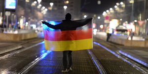 Ein Anhänger der Pegida-Bewegung steht mit einer deutschen Fahne in Dresden auf der Straße.