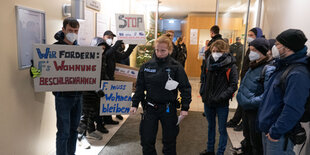 Menschen mit Masken stehen in einem Flur, einige halten Schilder hoch