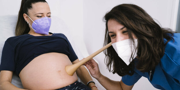 Eine Hebamme hört einer Schwangeren den Bauch ab