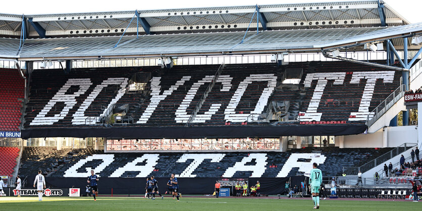 Eine leere Fußballtribüne, auf den Stuhlreihen ist der Schriftzug "Boycott Qatar" zu lesen