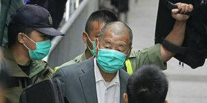 Jimmy Lai mit Mundschutz, um ihn herum Polizeibeamte ebenfalls mit Mundschutz, einer von ihnen hält ein Schutzschild hoch