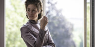 Vicky Krieps als Sissi in historischem Kleid steht vor einer modernen Fensterscheibe