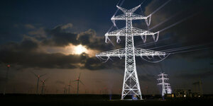 beleuchtete Strommasten vor dramatischem Abendhimmel und Windpark