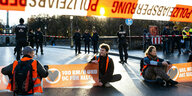 Junge Leute in Warnwesten blockieren sitzend eine Straße in München