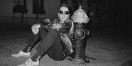 Joe Sttummer trägt eine Sonnenbrille in der Nacht und lehnt in Lederjacke an einem Hydranten