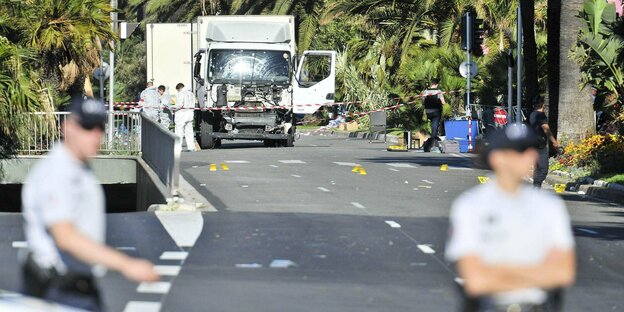Uniformierte sperren einen Tatort ab, im Hintergrund ein Lastwagen mit zerstörter Windschutzscheibe