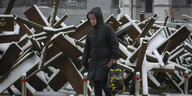 Frau in Wintermantel geht an schneebedeckten Panzerabwehrigeln vorbei