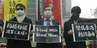 Drei Menschen halten Schilder auf einer Demonstration, Aufschrift „ Stand With Stand News“