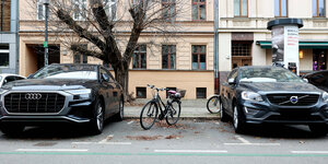 Ein Fahrrad auf einem Parkplatz steht zwischen zwei fetten Karren
