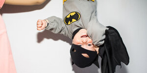 Ein Kleinkind im Batmankostüm hängt kopfüber