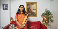 Meera Ramesh steht in einem orangefarbenen Sari vor einem roten Ledersofa