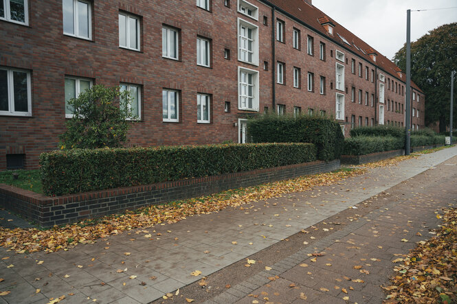 Wohnsiedlung mit geklinkerten Häusern, auf dem Gehweg etwas Laub - Herbststimmung