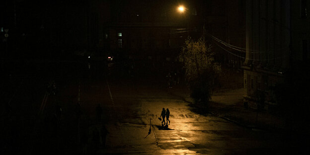 2 Menschen gehen während des Blackouts über eine Straße, nur eine Laterne leuchtet
