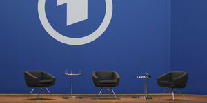 Leere Stühle vor einer blauen Wand mit dem Logo der ARD