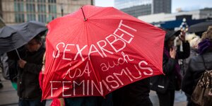 Menschen unter einem roten Regenschirm mit der Aufschrift " Sexarbeit ist auch Feminismus"