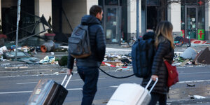 Menschen mit Rollkoffern laufen vor einem zerstörten Hotel