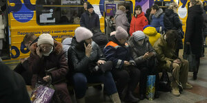 Menschen sitzen auf einem Bahnsteig vor einer U-Bahn
