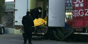 Unscharfes Foto zeigt wie zwei Arbeiter gelbe Leichensäcke in einen Lastwagen laden