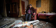 Eine ältere Frau sitzt in einem Sessel inmitten ihrer bei einem Raketenangriff zerstörten Wohnung