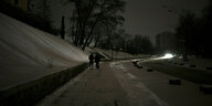 Eine dunkle Straße in Kyjiv, zwei Personen laufen auf dem Bürgersteig, in der Ferne ein Autolicht