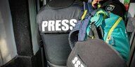 Aufnahme einer Pressekonferenz: Zu sehen sind Journalsiten mit Schutzkleidung
