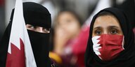Eine verschrieerte Frau und eine mit katarischer Schutzmaske auf der Tribüne im Stadion
