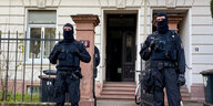 Polizisten mit Sturmhaube vor einem Haus.