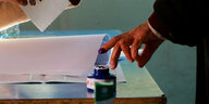 Ein Mann zieht seinen Finger aus einem blauen Tintenfass