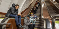 Menschen sitzen auf einer Rollstreppe und schauen in ihre Handys