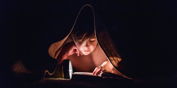 Ein Kind liest mit einer Taschenlampe unter der Bettdecke