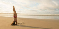 Eine Frau macht im Bikini Kopfstand am Meer im Sand