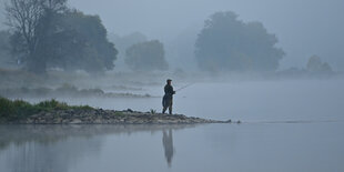 Ein Angler spiegelt sich im Wasser auf einer Buhne stehend