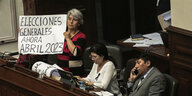 Im peruanischen Kongress hält eine Frau ein Schild hoch, auf spanisch dem "Generalwahlen jetzt im April 2023" steht