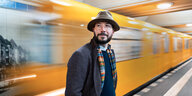Ein Mann mit Hut steht vor der gelben U-Bahn, die vorbeizieht